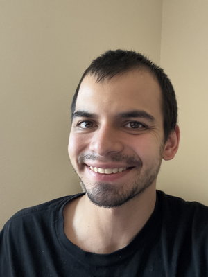 Smiling man with short dark hair and beard in black t-shirt.