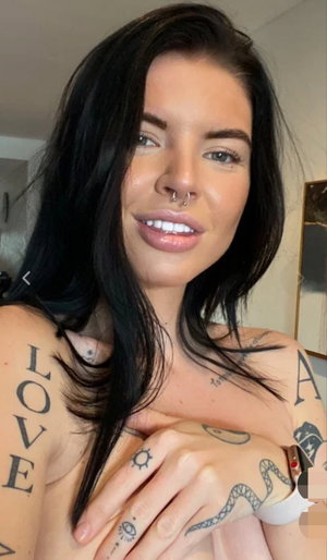 Woman with long black hair and tattoos posing indoors.