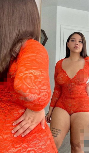 Woman in red lace bodysuit taking mirror selfie indoors.