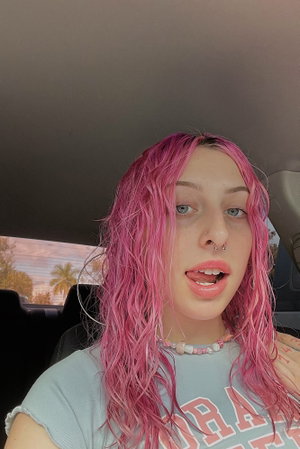 Woman with pink hair wearing t-shirt inside vehicle.
