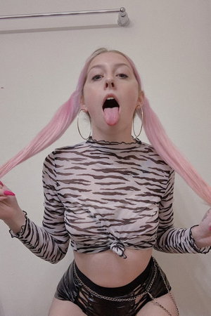 Woman with pink pigtails wearing zebra top and black shorts indoors.