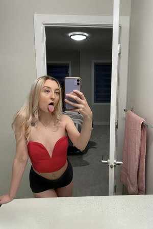 Blonde woman in red top taking mirror selfie indoors.