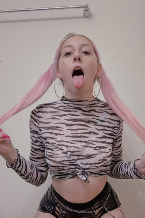 Woman with pink pigtails in zebra-print top and black shorts, posing indoors.