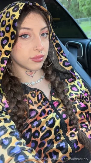 Woman with braided hair in leopard-print hoodie, sitting in car, wearing jewelry and nose ring.
