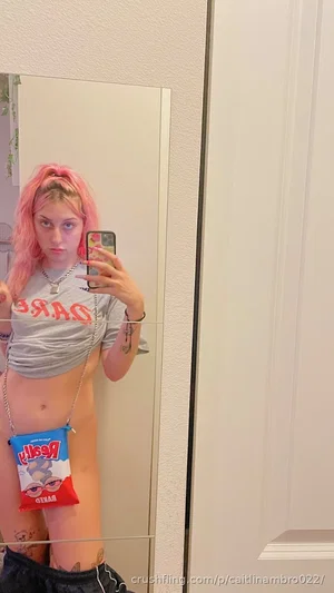 Woman with pink hair in mirror selfie, wearing crop top and shorts, holding phone.