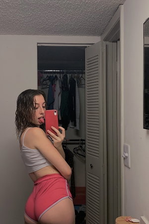 Woman in crop top and shorts taking mirror selfie indoors.