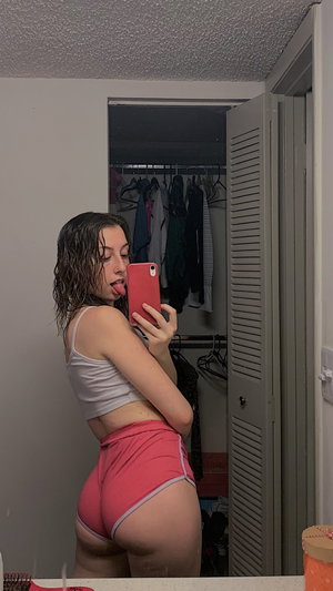 Woman in crop top and shorts taking mirror selfie indoors.