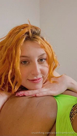Woman with orange hair in green top, posing indoors with hand on shoulder.