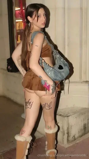 Woman in brown crop top and mini skirt with thigh tattoos, wearing fur boots and crossbody bag,
