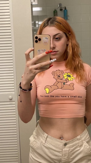 Redhead in pink crop top, white pants, bathroom mirror selfie.