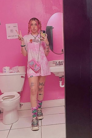 Woman with pink pigtails in short pink dress in bathroom mirror selfie.