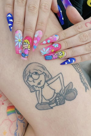 Close-up of hands with colorful nail art and cartoon tattoo on wrist.