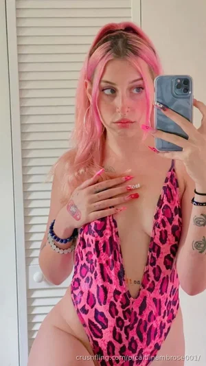 Woman with pink hair in leopard print swimsuit taking mirror selfie indoors.