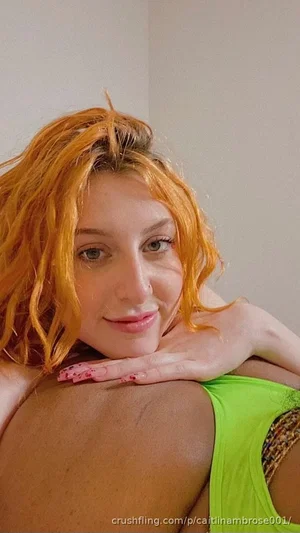 Woman with orange hair in green top resting head on shoulder, indoor setting.