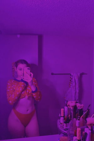 Woman taking mirror selfie in bathroom wearing orange crop top and bottoms.