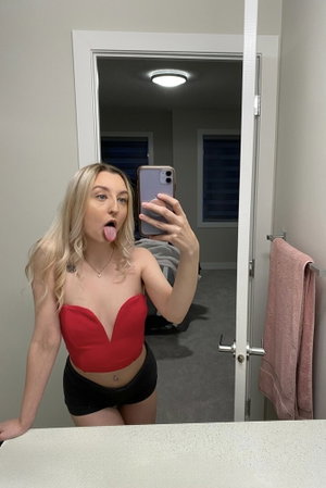 Blonde woman in red top taking mirror selfie indoors.