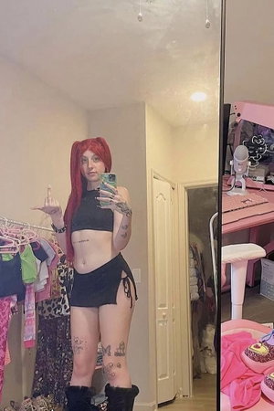Woman with red pigtails taking mirror selfie in bedroom.