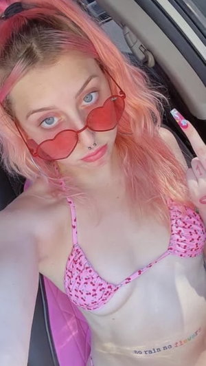 Woman with pink hair wearing bikini in car selfie.