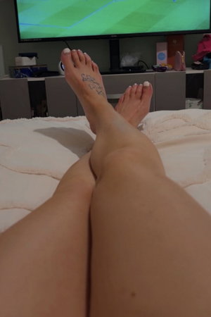Legs with foot tattoo on bed in front of TV.