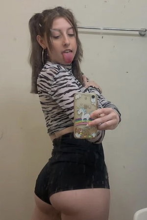 Woman in zebra top and black skirt taking bathroom mirror selfie.