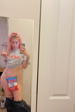 Woman with pink hair taking mirror selfie in crop top.