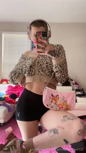 Woman in leopard crop top and black shorts, tattoos, pink rug, mirror selfie.