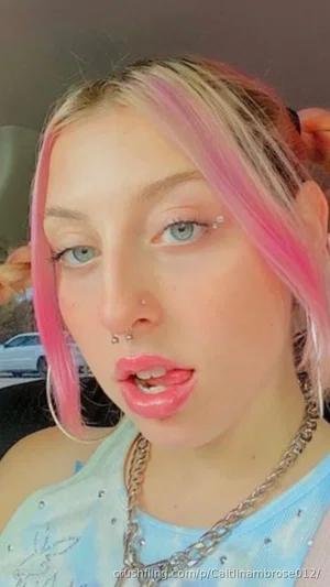 Woman with pink and blonde hair, wearing a light blue top and chain necklace, indoors.