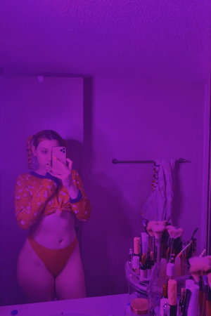 Woman taking mirror selfie in bathroom wearing orange outfit