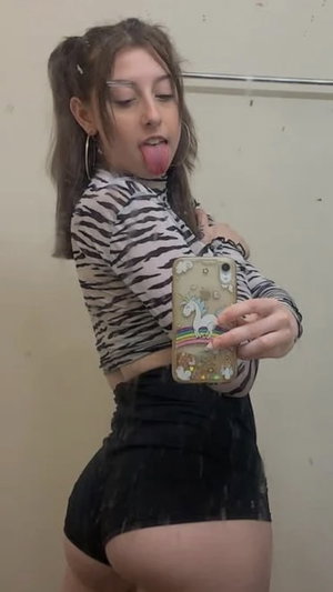 Woman in zebra top and black shorts taking selfie indoors.