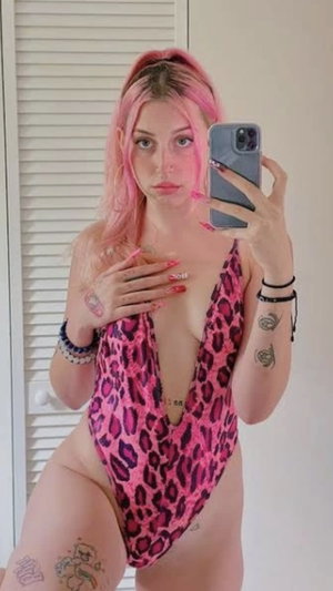 Pink-haired woman in leopard swimsuit, indoor selfie.