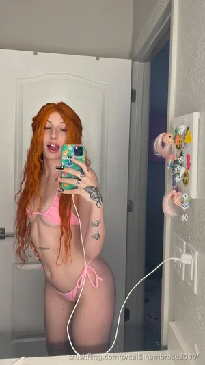 Woman with red hair in pink bikini takes mirror selfie in bathroom.