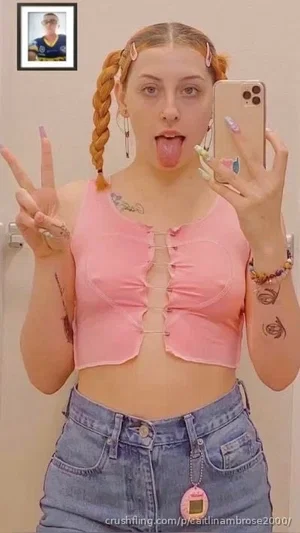Woman with braided hair in pink crop top and jeans, making peace sign and sticking out tongue in
