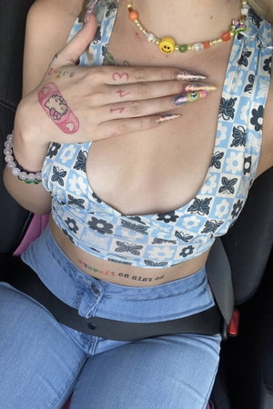 Woman with tattoos in floral crop top and jeans inside car.
