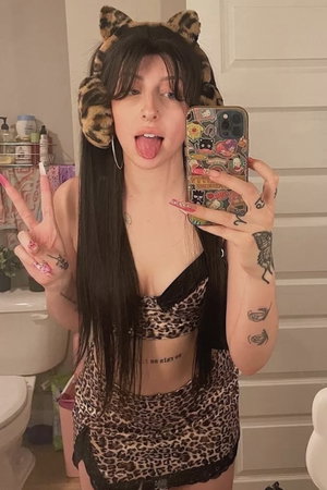 Woman with long dark hair in leopard outfit taking bathroom mirror selfie.