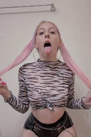 Woman with pink pigtails in sheer zebra top indoors.