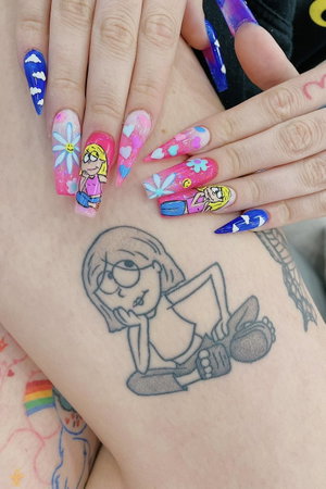 Close-up of hands with colorful nail art and cartoon tattoo on wrist.