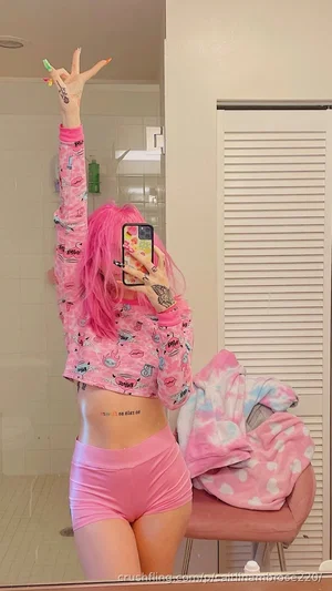 Woman with pink hair in pink pajamas taking mirror selfie in bedroom.