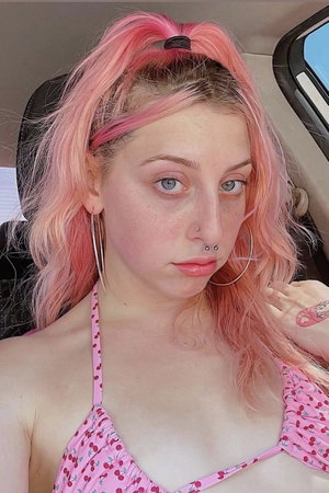 Woman with pink hair in cherry top taking selfie in car.