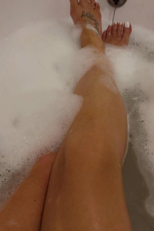 Legs and feet in bubbly bathtub with ankle tattoo.