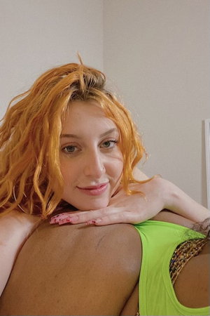 Woman with orange hair in green top resting head on shoulder, indoor setting.