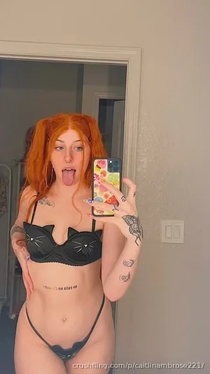 Woman with red hair in cat-themed lingerie taking mirror selfie indoors.