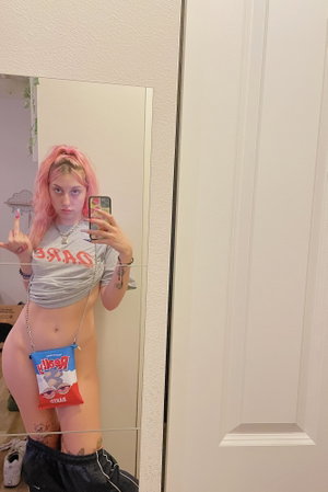 Pink-haired woman in crop top with chain bag taking mirror selfie.