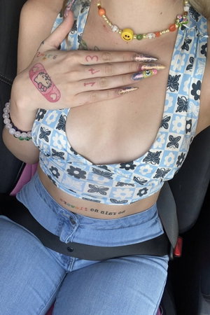 Woman with tattoos in floral crop top and jeans seated in car.