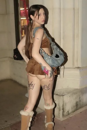 Woman with long brown hair in brown outfit and boots outdoors.