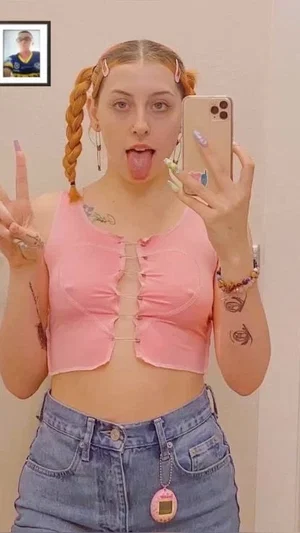 Woman with pigtails in pink crop top and jeans, making a playful face in mirror selfie.