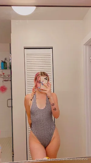 Woman in black and white checkered one-piece swimsuit taking mirror selfie in bathroom.