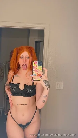 Woman with red hair in cat-ear bra and thong, taking mirror selfie indoors.