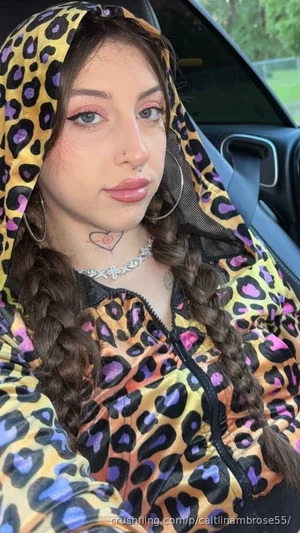 Woman with braided hair in leopard print hoodie, sitting in car, wearing jewelry and nose ring.