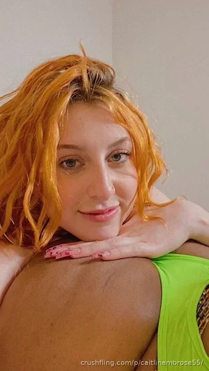 Woman with orange hair in green top, resting head on shoulder, indoor setting.