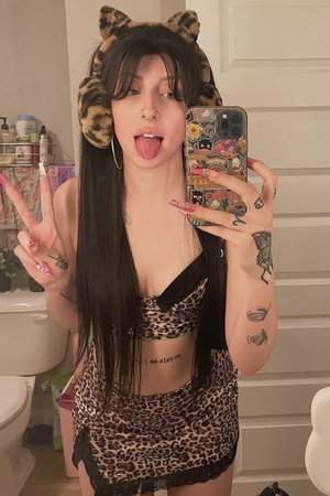 Woman with long dark hair in leopard print taking bathroom selfie.